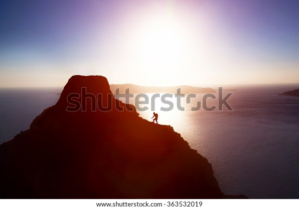 Man climbing up hill to reach the peak of the mountain\
over ocean. Persistence, determination, strength, reaching the\
target concepts. 