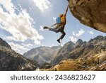 A man is climbing a mountain with a blue backpack. He is wearing a yellow jacket and is jumping off a cliff