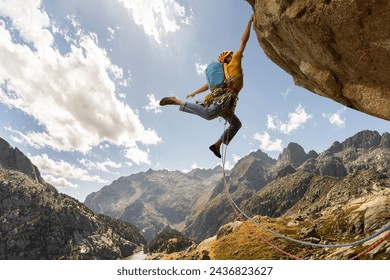 A man is climbing a mountain with a blue backpack. He is wearing a yellow jacket and is jumping off a cliff - Powered by Shutterstock