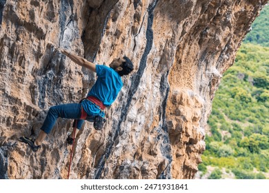 A man is climbing a rock wall with a blue shirt on. Concept of adventure and excitement as the man conquers the challenging climb - Powered by Shutterstock