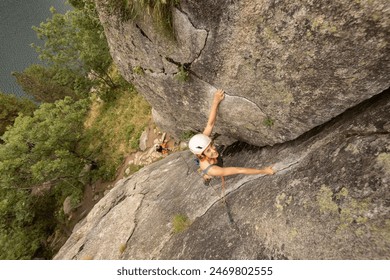 A man is climbing a rock wall with a helmet on. Concept of adventure and excitement as the man takes on the challenge of scaling the steep rock face - Powered by Shutterstock