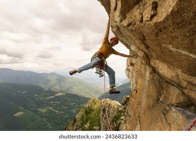 A man is climbing a rock wall with a yellow shirt and orange helmet. Concept of adventure and excitement, as the man is taking on a challenging and thrilling activity - Powered by Shutterstock