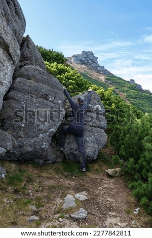 A man climbs mountains. A man is climbing a large rock. The tourist climbs the mountains. Vertical frame.