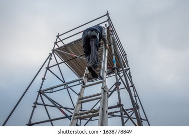 A Man Climbs Onto Scaffolding On An Extension Ladder