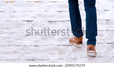Man climbs snow covered staircase. Person climbing slippery snowy stairs. Man walks up stairs with snow steps. Dangerous winter walking. Stair accidents concept
