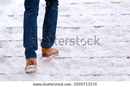 Man climbs snow covered staircase. Person climbing slippery snowy stairs. Man walks up stairs with snow steps during snowfall. Dangerous winter walking. Stair accidents concept
