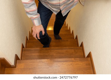 A man climbs the stairs with his hand on his knee - Powered by Shutterstock