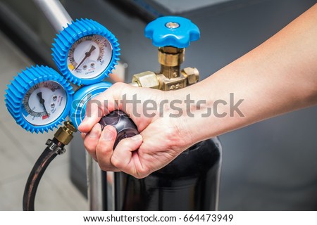 Man close operating valve of welding equipment acetylene gas cylinder with pressure gauges on the oxygen tank.