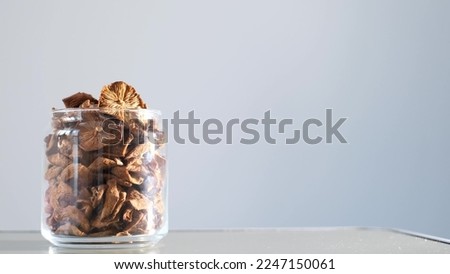 A man closes a jar of dried mushrooms on a gray background. Organically pure mushrooms collected in the forest. Vegan food concept