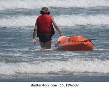 Man with cloth hat carrying kayak on the beach among the waves - Powered by Shutterstock