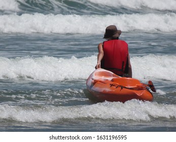 Man with cloth hat carrying kayak on the beach among the waves - Powered by Shutterstock