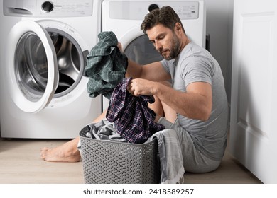 Man with clothes near washing machine. Laundry cleaning. Housework, homework, male housekeeper. Husband man doing laundry at home. Washer and dryer at home. - Powered by Shutterstock