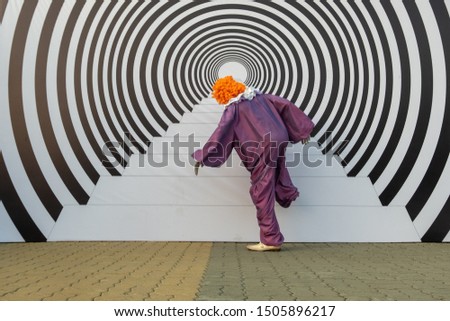 A man in a clown costume pretends to be climbing stairs. Hypnotic effect and optical illusion. 3d picture on the street in the form of steps and concentric circles.