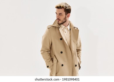 man in coat holds hands in pockets fashion modern style look aside light background