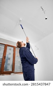 Man coating ceiling surface with paint roller during renovation. Fresh white layer for clean interior look, construction work and residential improvement concept