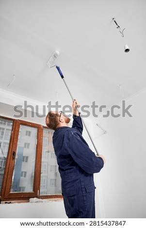 Man coating ceiling surface with paint roller during renovation. Fresh white layer for clean interior look, construction work and residential improvement concept