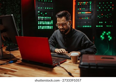 Man coding or hacking on a red laptop in a dark data center, surrounded by busy blinking server rack lights - Powered by Shutterstock - Get 15% off with code: PIKWIZARD15