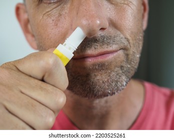 Man With A Cold Has A Menthol Inhaler Stuck Up His Nostril. Background Is Blurred.