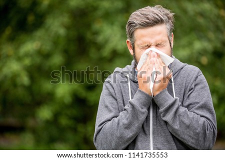Man with cold or hay fever sneezing using tissue to clean nose