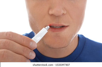 Man With Cold Sore Applying Cream On Lips Against White Background, Closeup