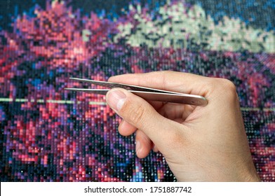 Man collect diamond painting. Diamond embroidery with a tweezers. Acrylic rhinestones. Closeup, selective focus