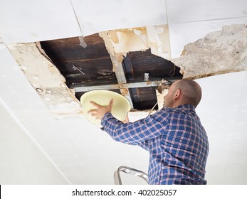  Man Collecting Water In basin From Ceiling. Ceiling panels damaged  huge hole in roof from rainwater leakage.Water damaged ceiling .  
