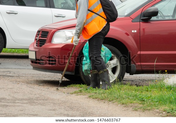 A man collects garbage from the\
lawns in a package, parked next to the car white and\
red.