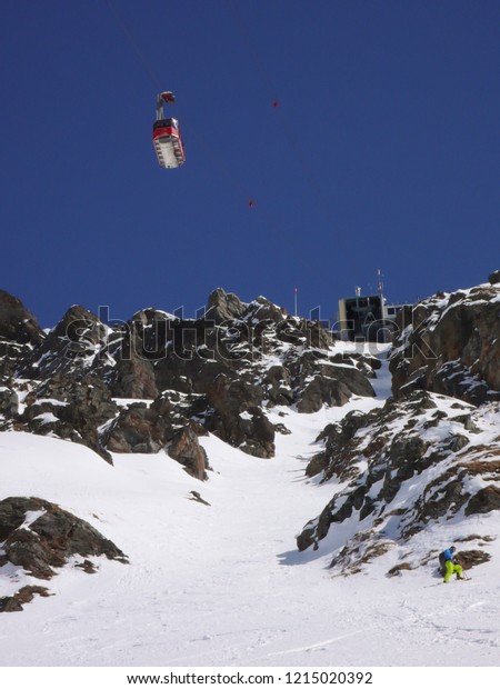 man in\
colorful outfit skiiing down a very steep snow couloir under a\
cable car station in the Swiss Alps in deep\
winter
