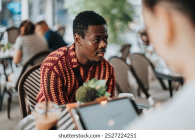 Man in a colorful shirt having a focused conversation at a trendy outdoor cafe. Casual yet intense interaction in a social setting. - Powered by Shutterstock