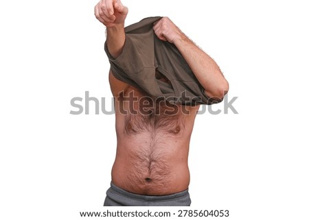 Man in comfortable long johns layers up by pulling on a soft cotton t-shirt. Simple dressing moment: man in traditional long johns pulls casual t-shirt over his head.