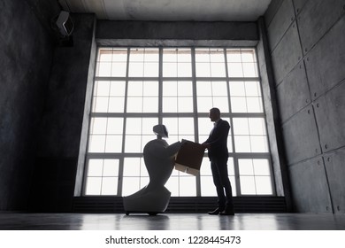 A man communicates with a robot, with cardboard box in hand. delivery concept. silhouette of the robot against the window