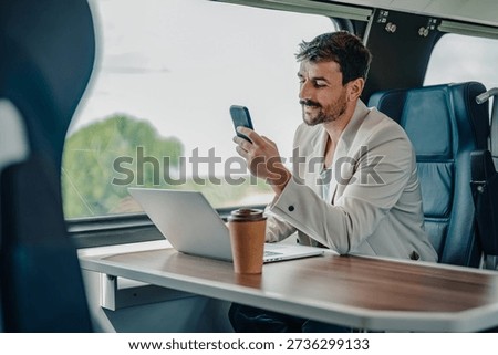 Man commuting by train, looking at smartphone and working on laptop. Blending travel, business, and modern technology