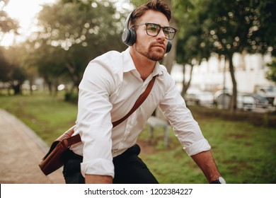 Man commuting to office on a bicycle early in the morning. Man wearing office bag and wireless earphones riding a bicycle. - Powered by Shutterstock