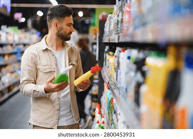 Man comparing two spray bottles of cleaning products in a bright supermarket aisle, making a selection for household needs