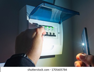 A man in complete darkness, is using a smartphones flashlight to investigate and switches ON residual current device (RCD) consumer unit in an automatic fuse box during a electric power outage at home