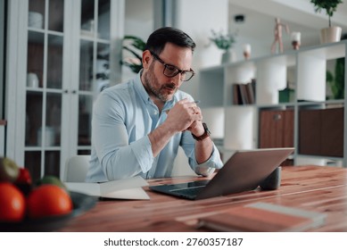 Man concentrating, deep in thought while working on a laptop at his home office desk. Representing focused work and productivity