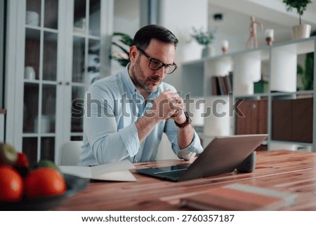 Man concentrating, deep in thought while working on a laptop at his home office desk. Representing focused work and productivity