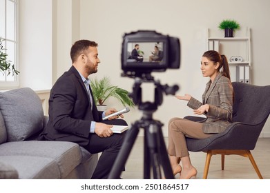 Man is conducting an interview with a woman, recording it with a video camera or broadcasting live. Tv interview, news show, talk show or pr event. Reporter engaged in conversation with woman. - Powered by Shutterstock