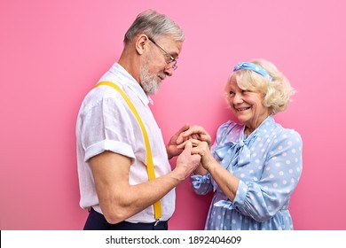 man confesses his feelings to wife isolated on pink background, gray-haired couple in love. man holding woman's hands