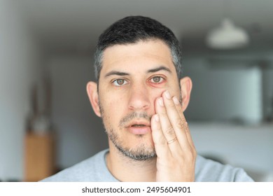 Man with conjunctivitis looking directly to the camera with hand on face