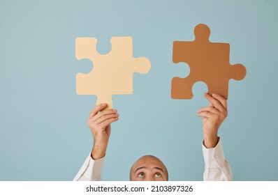 Man connecting two puzzle parts that match perfectly. Cropped shot of young guy holding up brown and beige paper jigsaw pieces on blue background. Integration, education, problem solving concept