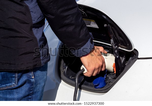 A man connects\
charging to an electric car.