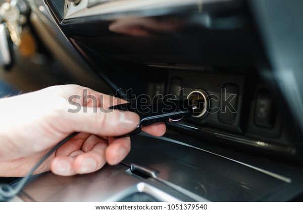 A man connects the device\
to the cigarette lighter of the car. The man\'s hand is plugging the\
car camera or phone adapter into the cigarette lighter into the\
car.