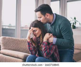 Man Consoling Sad Girl At Home With Hug, Kiss And His Presence