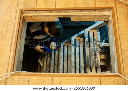 A man with construction tools performs engineering work in the basement of a house.