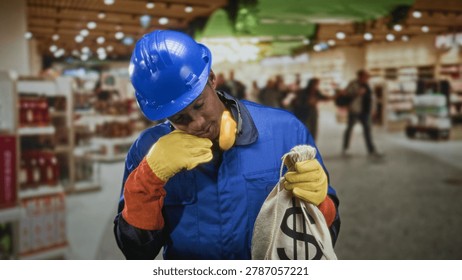 Man construction worker adjusts ear protection while holding a money bag in a retail building aisle; tired temptation.