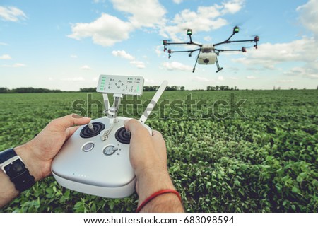 The man control octocopter or remote control for the drone in the hands for take a picture on sky. Agriculture drone flies over the green field.
