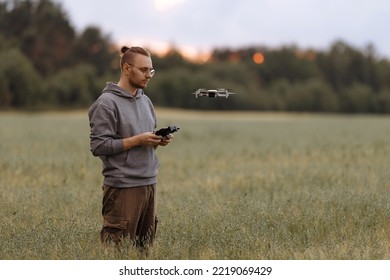 Man Controlling A Drone With A Remote Control Stands In A Field. Drone Operator. Aerial Photography. Recording Footage In The Air. New Technologies And Trends In Photo And Video Shooting.