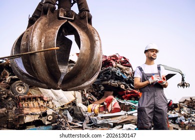 Man controlling process of industrial scrap metal recycling at junk yard.