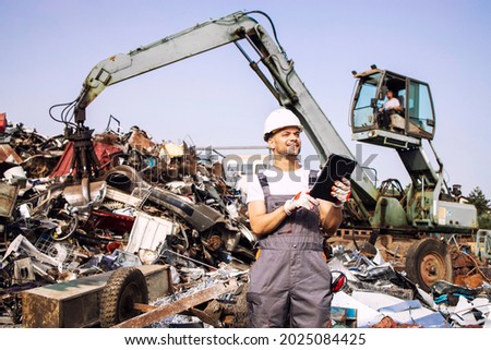 Man controlling process of industrial scrap metal recycling at junk yard.